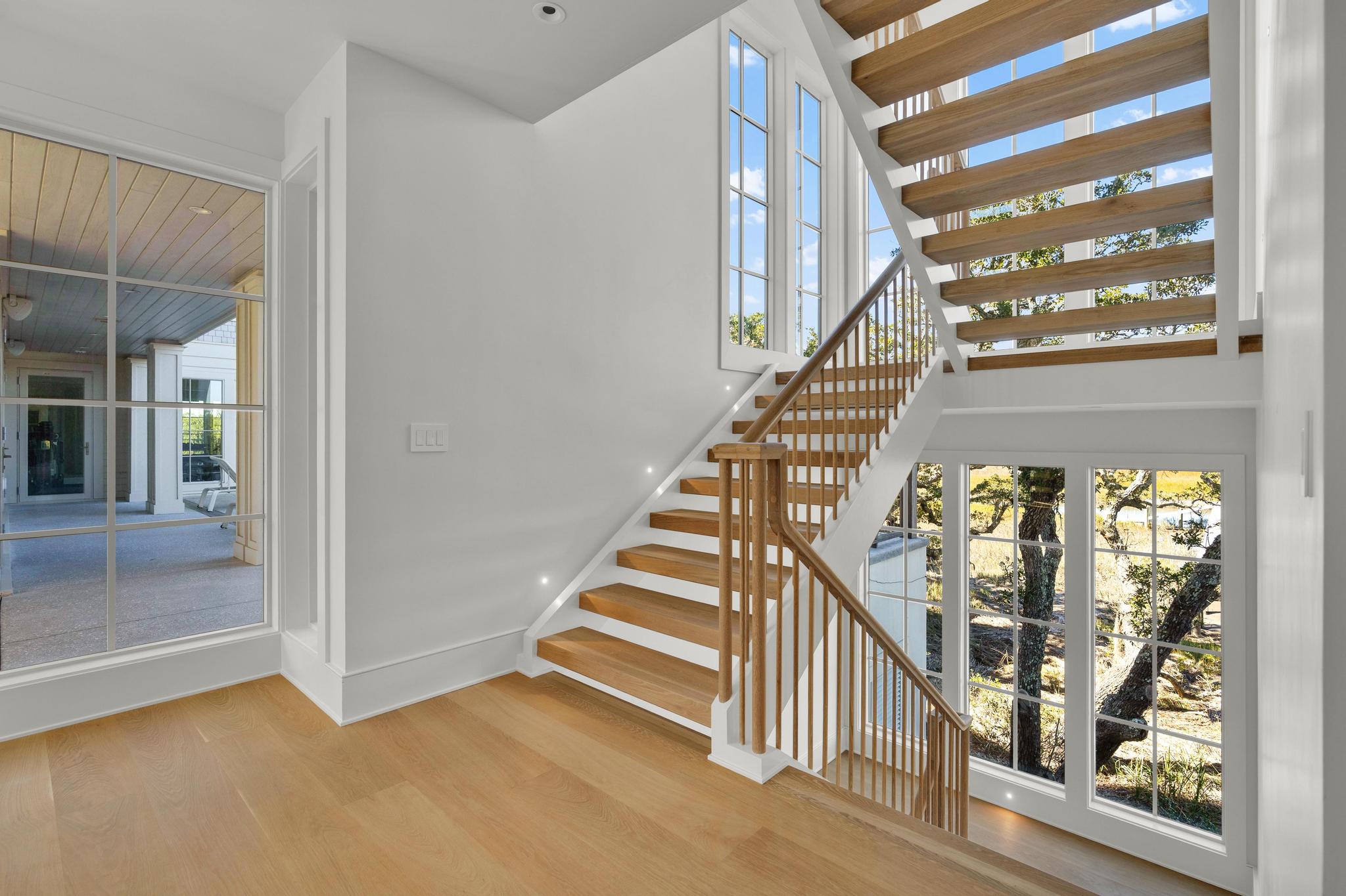 Stair hall with open oak treads and tall windows over the marsh